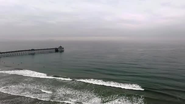 Drohne fliegt über Wellen und Surfer auf Seebrücke zu — Stockvideo