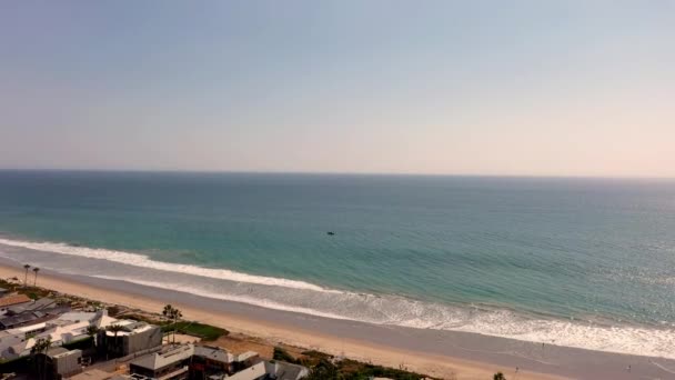 Drone flies over beach front homes in Malibu with sailboat on ocean — Stock Video