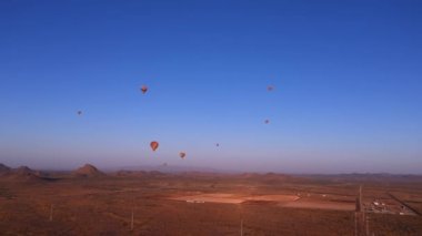 Renkli sıcak hava balonları dağların üzerinde uçuyor ve güneş doğarken çöl manzarası