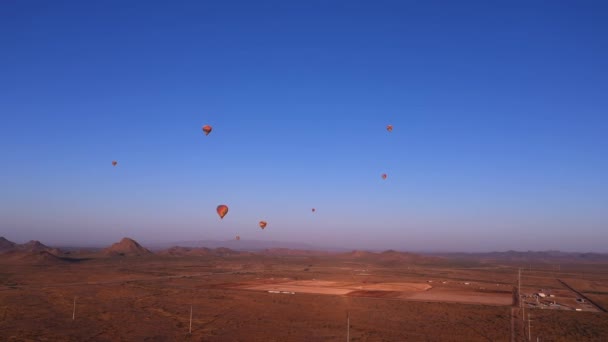 Bunte Heißluftballons fliegen bei Sonnenaufgang über Berge und Wüstenlandschaft — Stockvideo