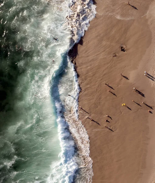 Vista dall'alto verso il basso di persone che proiettano ombre sulla spiaggia sabbiosa con onde oceaniche — Foto Stock
