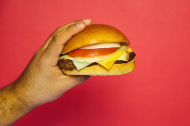Peynirli et burger. Büyük, güçlü ve sert elleri olan bir adam tarafından tutuluyor. Kırmızı zıt arkaplan ile.