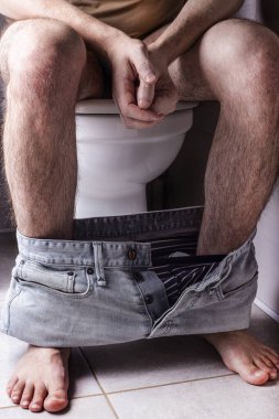 Evdeki ya da oteldeki klozette elinde tuvalet kağıdı olan bir adam. Karın ağrısı, kabızlık ya da ishal gibi şeyler. Adam elinde tuvalet kağıdı tutuyor.
