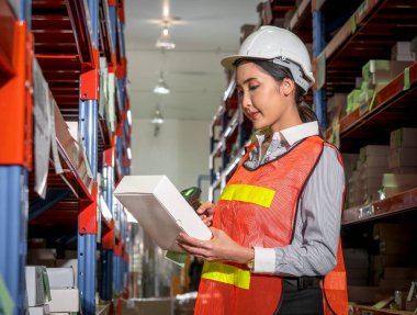 Üniformalı, kendine güvenen bir kadın depo çalışanının portresi. Deponun içindeki çalışma ortamında bir ürün tarayıcısı tutuyor..