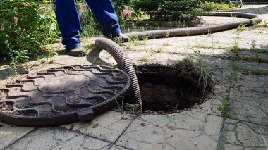 Çukurdan su pompalamak için kanalizasyon deliğine bir hortum indiriliyor. Kanalizasyon çukurunun temizlenmesi. Özel bir evde bakım ve bakım
