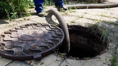 İşçi lağım kapağını açtı ve lağım çukurunu temizlemek için bir hortum yerleştirdi. Özel bir evde iletişimin bakımı. kirli iş