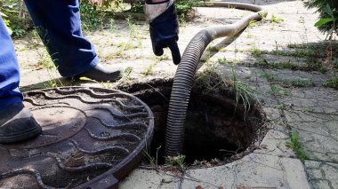 İşçi lağım kapağını açtı ve lağım çukurunu temizlemek için bir hortum yerleştirdi. Özel bir evde iletişimin bakımı. kirli iş
