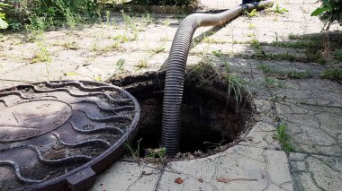 Çukurdan su pompalamak için kanalizasyon deliğine bir hortum indiriliyor. Kanalizasyon çukurunun temizlenmesi. Özel bir evde bakım ve bakım
