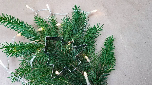 Noel ağacı şeklindeki kurabiye kalıbı köknar dallarının üzerinde yatar. Noel çelengi yanıyor. kış tatili geçmişi — Stok fotoğraf