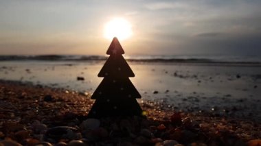 Deniz dalgaları ve günbatımının arka planındaki Noel ağacı. Kumsalda Noel. Sıcak ülkelerde kış tatili. Yeni yıl tatili.