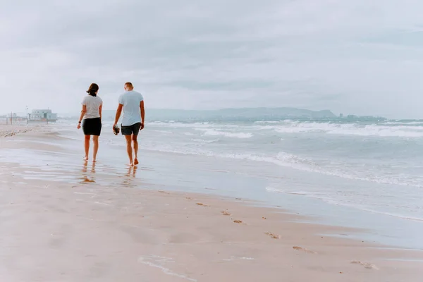 Two people-a man and a woman-are walking barefoot on a sandy beach.Rear view Of summer seascape with sea and sandy beach. A couple in love strolling along the beach.image in pastel colors — Stock Photo, Image