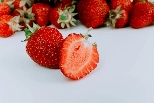 Fresh strawberries on a white background. Two sliced strawberries on the background of a hill of strawberries. Group of ripe strawberries with green leaves close-up. Ingredients for juice. — Stock Photo, Image