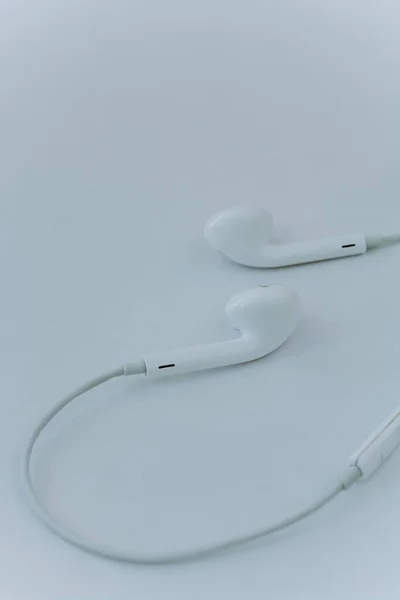 in-ear headphones are wired. White wired headphones lie on a white background. The concept of modern technologies and gadgets. Minimalism, close-up. vertical photo