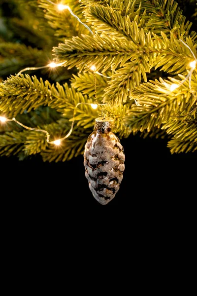 Um brinquedo de árvore de Natal pinecone nos ramos verdes da árvore. Luzes brilhantes guirlandas nos ramos de uma árvore de Natal. foto vertical — Fotografia de Stock