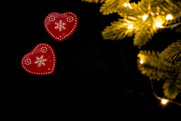 Dois corações de cerâmica vermelha em um fundo preto com luzes brilhantes guirlandas. Os valentim estão com ramos de abeto e guirlandas de luzes. Dia dos Namorados cumprimentando conceito. para os amantes — Fotografia de Stock