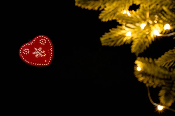 Um coração vermelho em um fundo preto com luzes brilhantes guirlandas. Valentine encontra-se com ramos de abeto e luzes guirlandas. Dia dos Namorados cumprimentando conceito. foto horizontal para os amantes — Fotografia de Stock