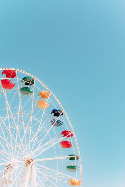 Güneşli bir günde mavi gökyüzü arka planında dönme dolaplar. Gökyüzüne karşı dönme dolabın renkli parlak kabini. Yazın parkta yeşil, sarı, mavi ve kırmızı renkli eğlenceli sürüşler.