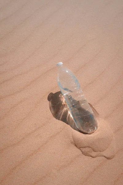 Uma garrafa de água em close-up na areia amarela, saciando sua sede em um dia quente de verão. Uma garrafa de plástico de água fria deixada na areia. em cores pastel. Foto vertical — Fotografia de Stock