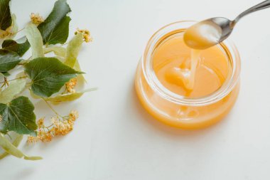 a glass jar of honey with linden flowers on a white background.The concept of healthy eating. Treatment of colds with honey. horizontal image