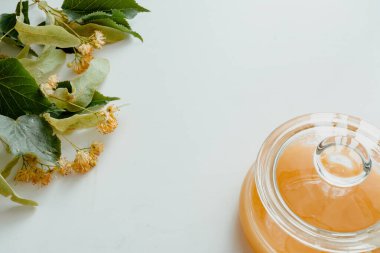a glass jar of honey with linden flowers on a white background.The concept of healthy eating. Treatment of colds with honey. horizontal image