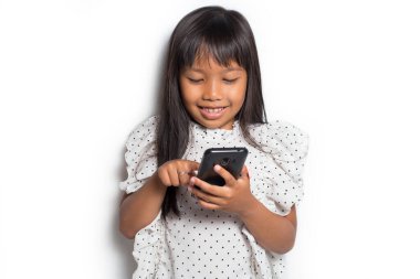 Mutlu Asyalı küçük kız beyaz arka planda akıllı telefon kullanıyor.