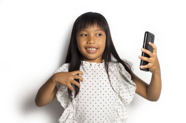 Mutlu Asyalı küçük kız beyaz arka planda akıllı telefon kullanıyor.