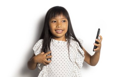 Mutlu Asyalı küçük kız beyaz arka planda akıllı telefon kullanıyor.