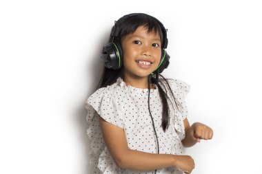 Kulaklıklı Asyalı küçük kız müzik dinliyor ve beyaz arka planda dans ediyor.