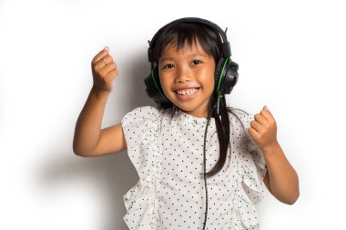 Kulaklıklı Asyalı küçük kız müzik dinliyor ve beyaz arka planda dans ediyor.