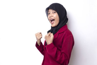 Başörtüsü takan Asyalı kadın zaferi kutlarken mutlu ve heyecanlı. Büyük başarı, güç, enerji ve pozitif duyguları ifade ediyor. Beyaz arka planda neşeli bir şekilde izole edilmiş yeni işi kutlar