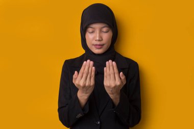 Sarı arka planda dua eden tesettürlü genç Asyalı Müslüman kadın.