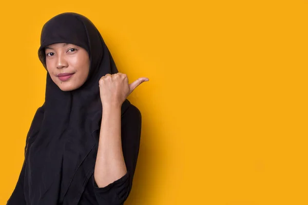黄色の背景にヒジャーブを身に着けている若いアジアのビジネス女性は 異なる方向に指で自信を持って指して笑っています 広告のコピースペース — ストック写真