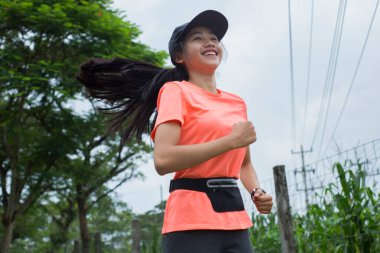 Genç Asyalı bir kadının portresi. Parkta egzersiz yapıyor, koşuyor.