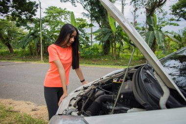 Asyalı kadın yolda bozuk arabayı kontrol ediyor.