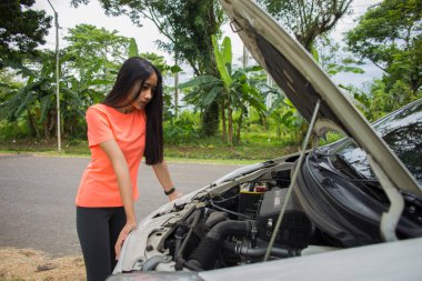 Asyalı kadın yolda bozuk arabayı kontrol ediyor.