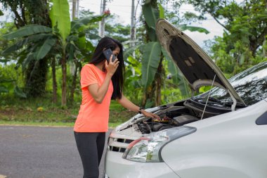 Asyalı kadın yolda bozuk arabayı kontrol ediyor.