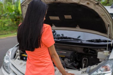 Asyalı kadın yolda bozuk arabayı kontrol ediyor.