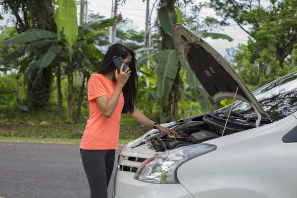 Asian woman checking broken down car on street