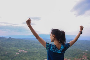 Dağ zirvesinde kollarını açmış tezahürat yapan genç kadın