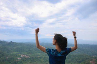 Dağ zirvesinde kollarını açmış tezahürat yapan genç kadın