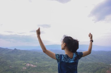 Dağ zirvesinde kollarını açmış tezahürat yapan genç kadın