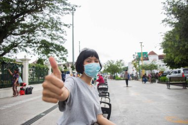  Korumacı tıbbi maske takan Asyalı kız halka açık yerlerde jest yapıyor.