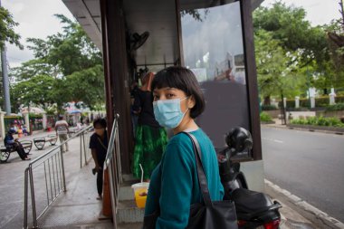 Sağlık maskeli Asyalı kadın, otobüs durağında bekliyor.