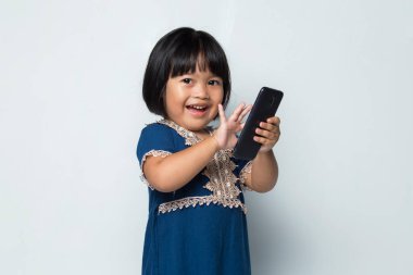 Mutlu Asyalı küçük kız beyaz arka planda akıllı telefon kullanıyor.
