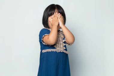 Korkan Asyalı küçük kız ellerini beyaz arka planda tutuyor.