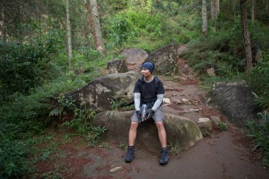 Yürüyüş yapan adam dağlarda yürüdükten sonra şişeden su içiyor ve dinleniyor. 