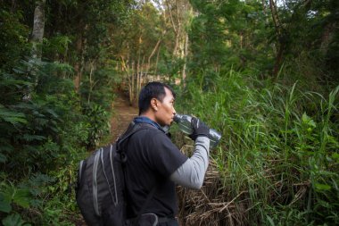 Yürüyüş yapan adam dağlarda yürüdükten sonra şişeden su içiyor ve dinleniyor. 