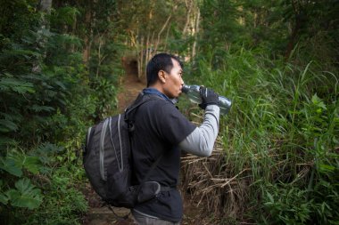Yürüyüş yapan adam dağlarda yürüdükten sonra şişeden su içiyor ve dinleniyor. 