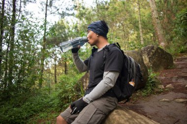 Yürüyüş yapan adam dağlarda yürüdükten sonra şişeden su içiyor ve dinleniyor. 