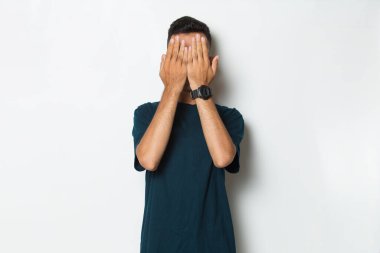 Genç yakışıklı adam ellerini beyaz arka planda izole bir şekilde yüzünü kapatıyor.